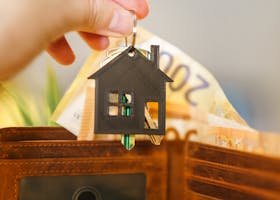 A hand holds a house-shaped keychain above an open wallet with Euro banknotes.