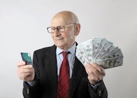 Elderly man in a suit holding a credit card and US dollar bills, representing finance and wealth.